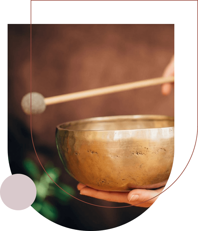 Close-up of a person holding a brass singing bowl and a mallet, ready to produce sound, often used in spiritual courses.