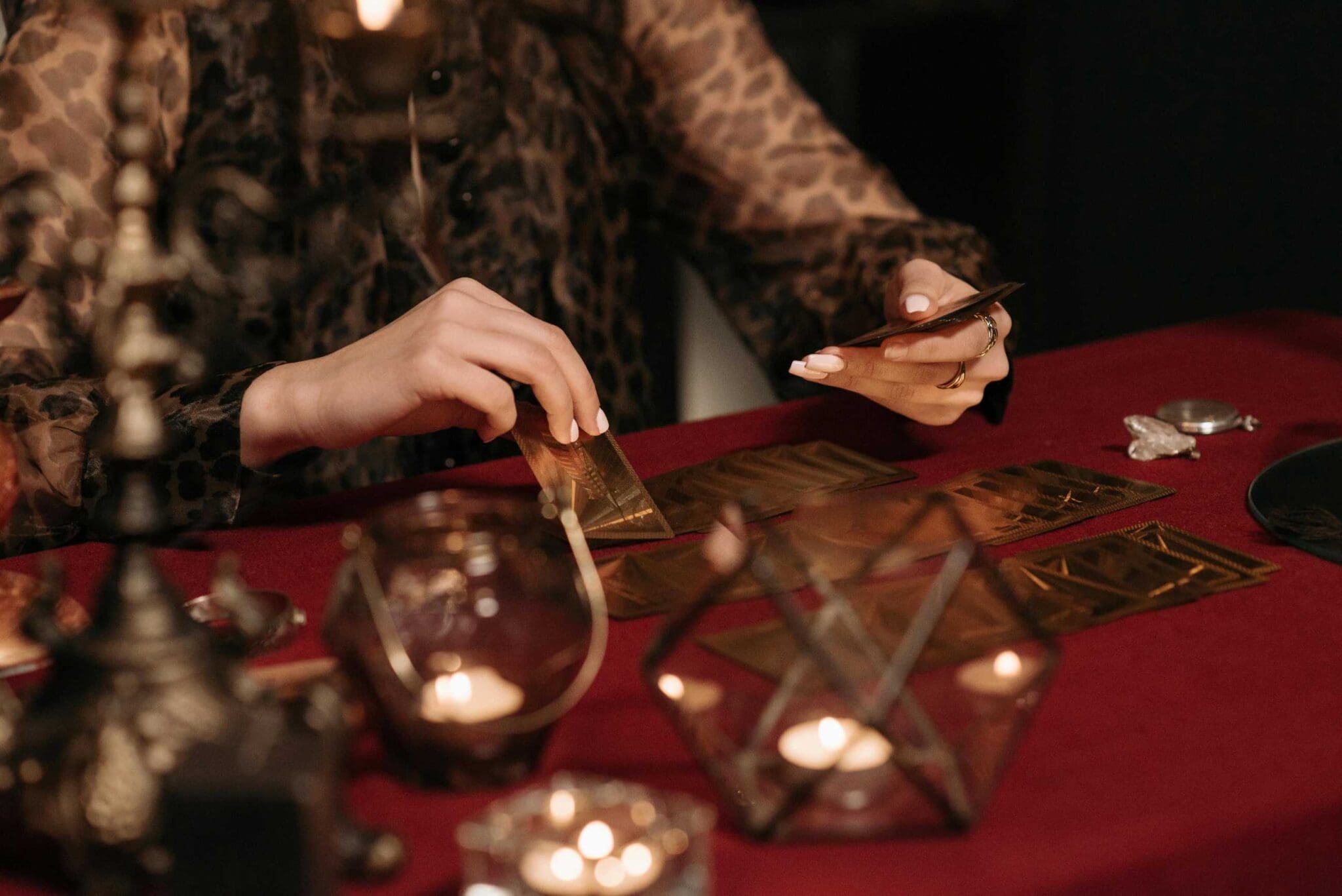 A person is laying out tarot cards on a red tablecloth surrounded by candles and ornate items.