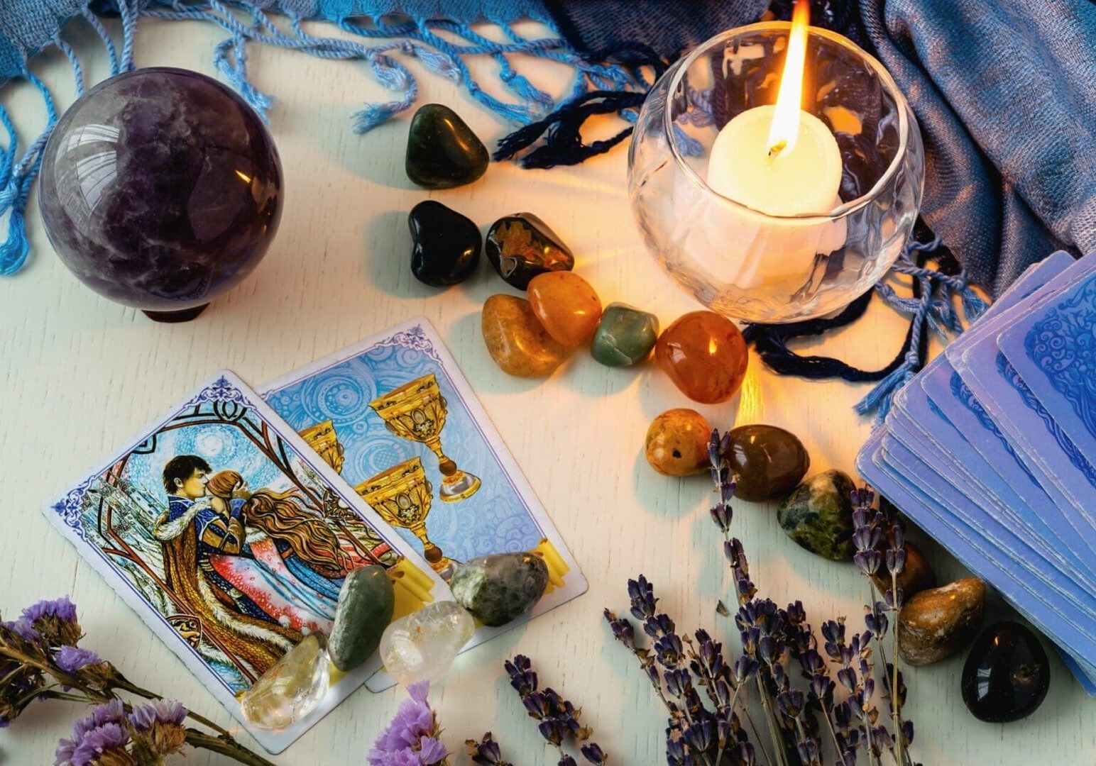 Minsk, Belarus - February 2022: cards of goblets and lovers in tarot divination with candles and stones on a light table with dried flowers and a blue tablecloth. Magic and the occult