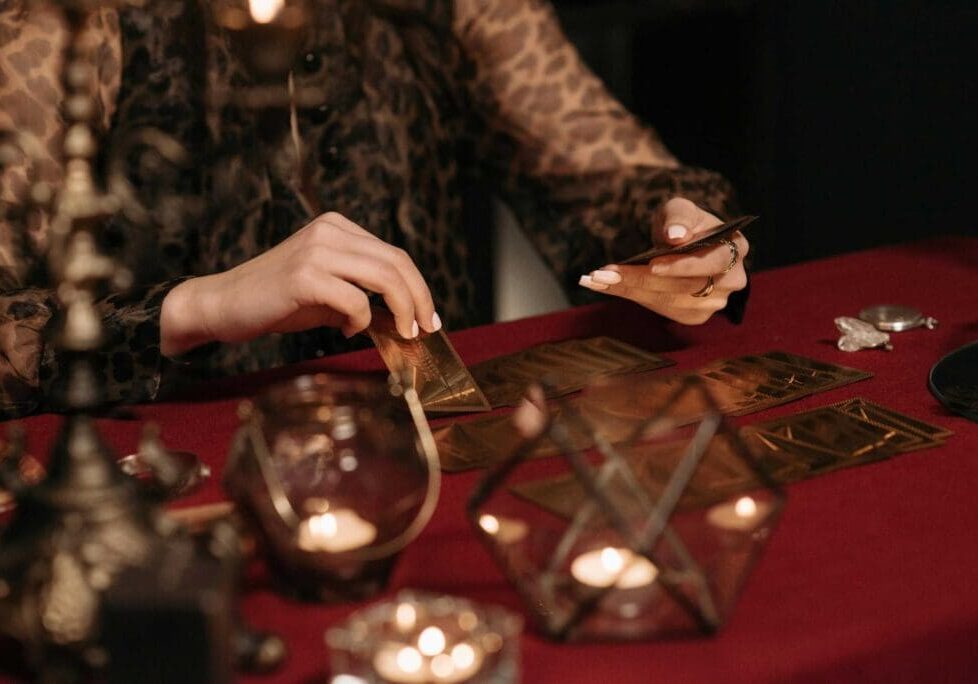 A person is laying out tarot cards on a red tablecloth surrounded by candles and ornate items.